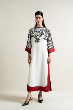 Woman wearing a white dress with black floral patterns and red accents on a plain background
