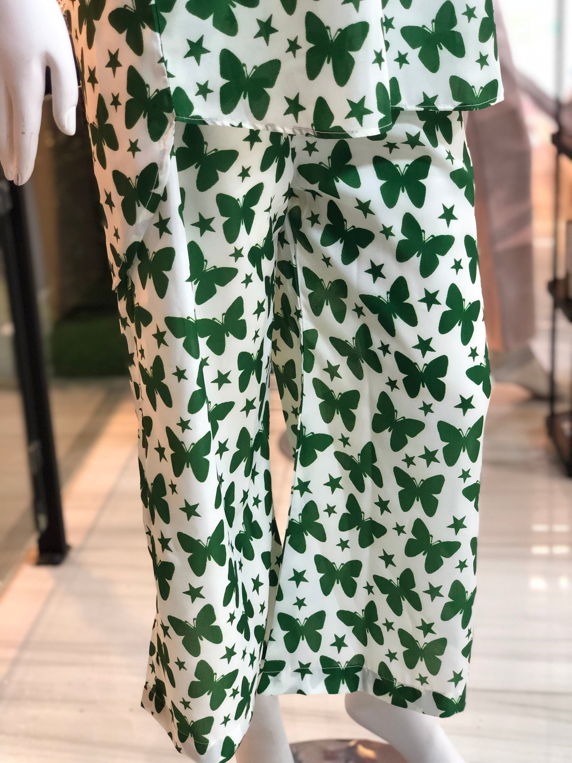 Green butterfly patterned pants on a mannequin against a blurred indoor background
