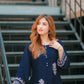 Woman in a navy blue dress with white embroidery standing on metal stairs.