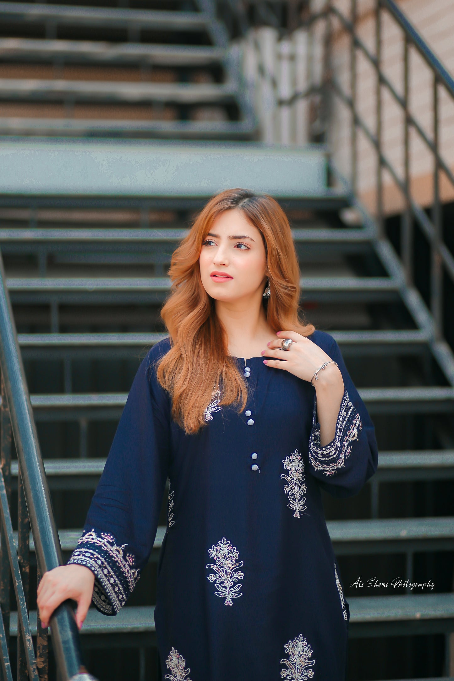 Woman in a navy blue dress with white embroidery standing on metal stairs.