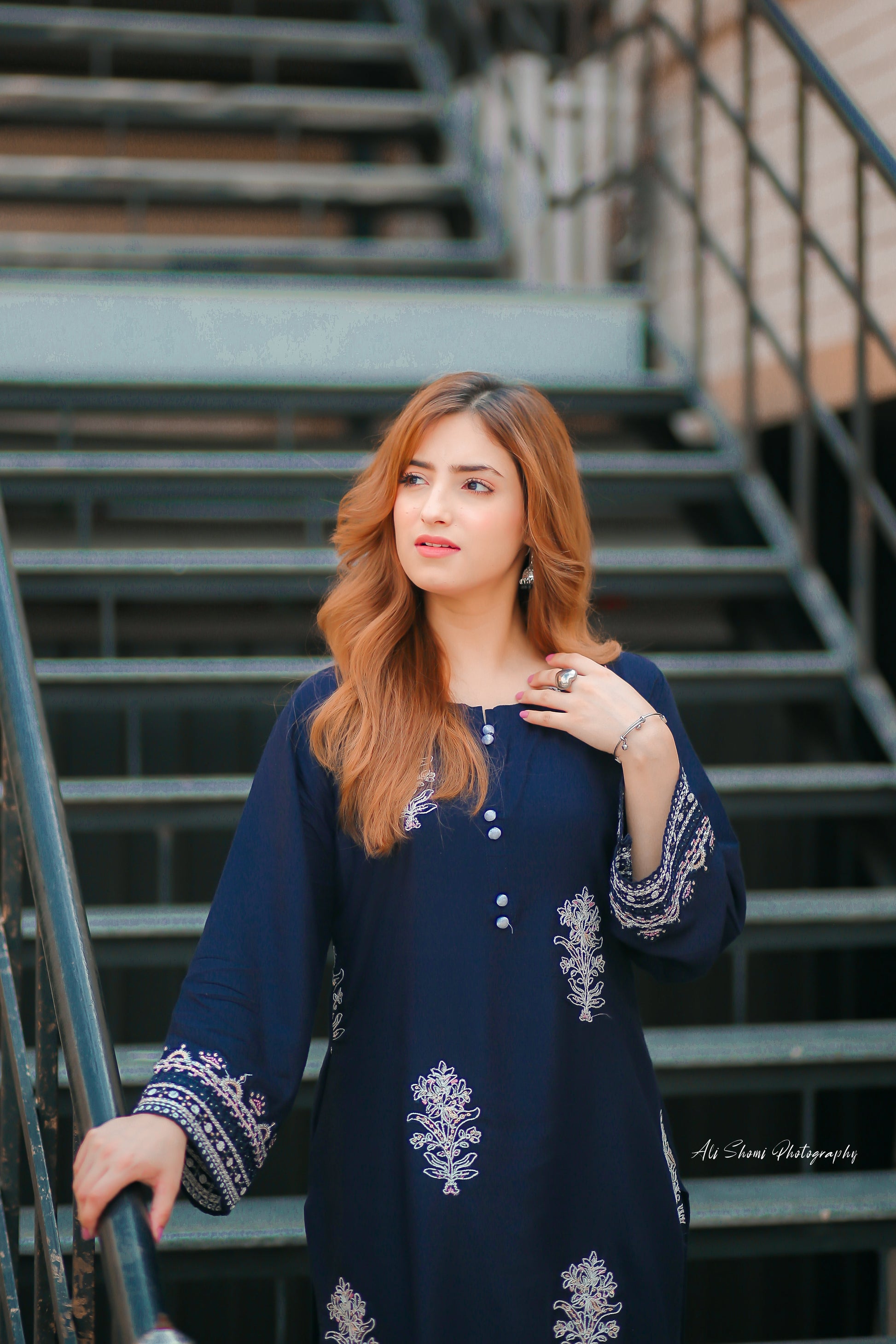 Woman in a navy blue dress with white embroidery standing on metal stairs.