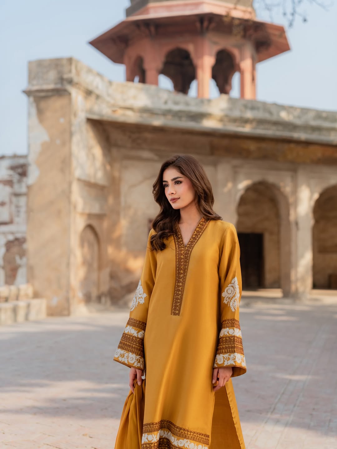 Woman in a yellow dress standing in front of an architectural structure.