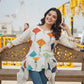 Woman sitting on a bench wearing a colorful top with geometric patterns.