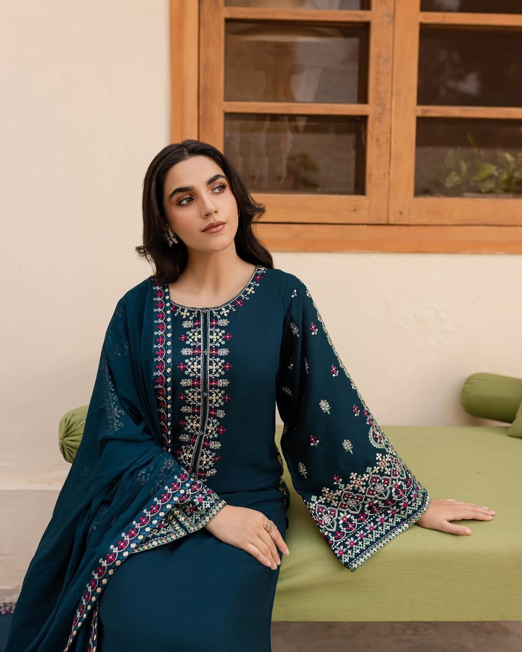 Woman in a dark blue embroidered traditional outfit sitting on a green chair.
