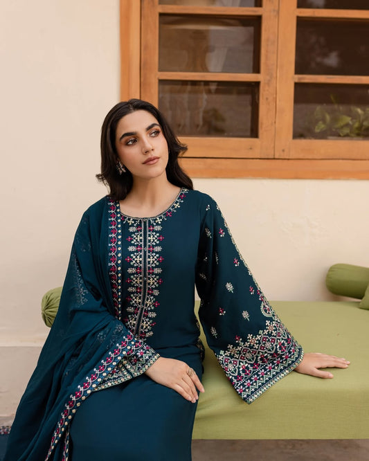 Woman in a dark blue embroidered traditional outfit sitting on a green chair.