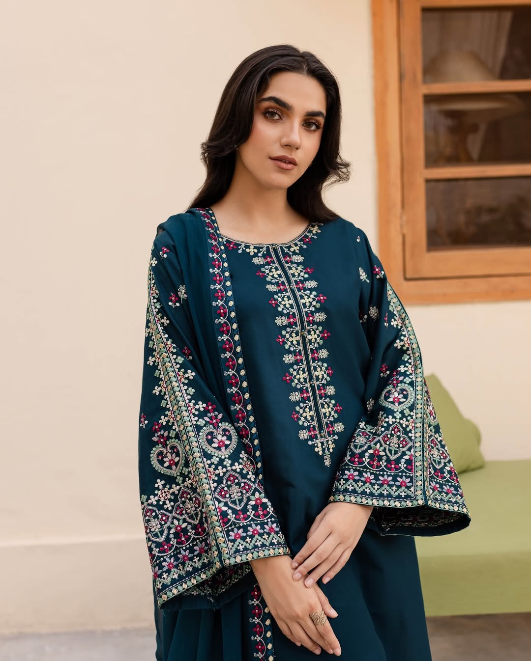 Woman wearing a teal embroidered outfit in an indoor setting.
